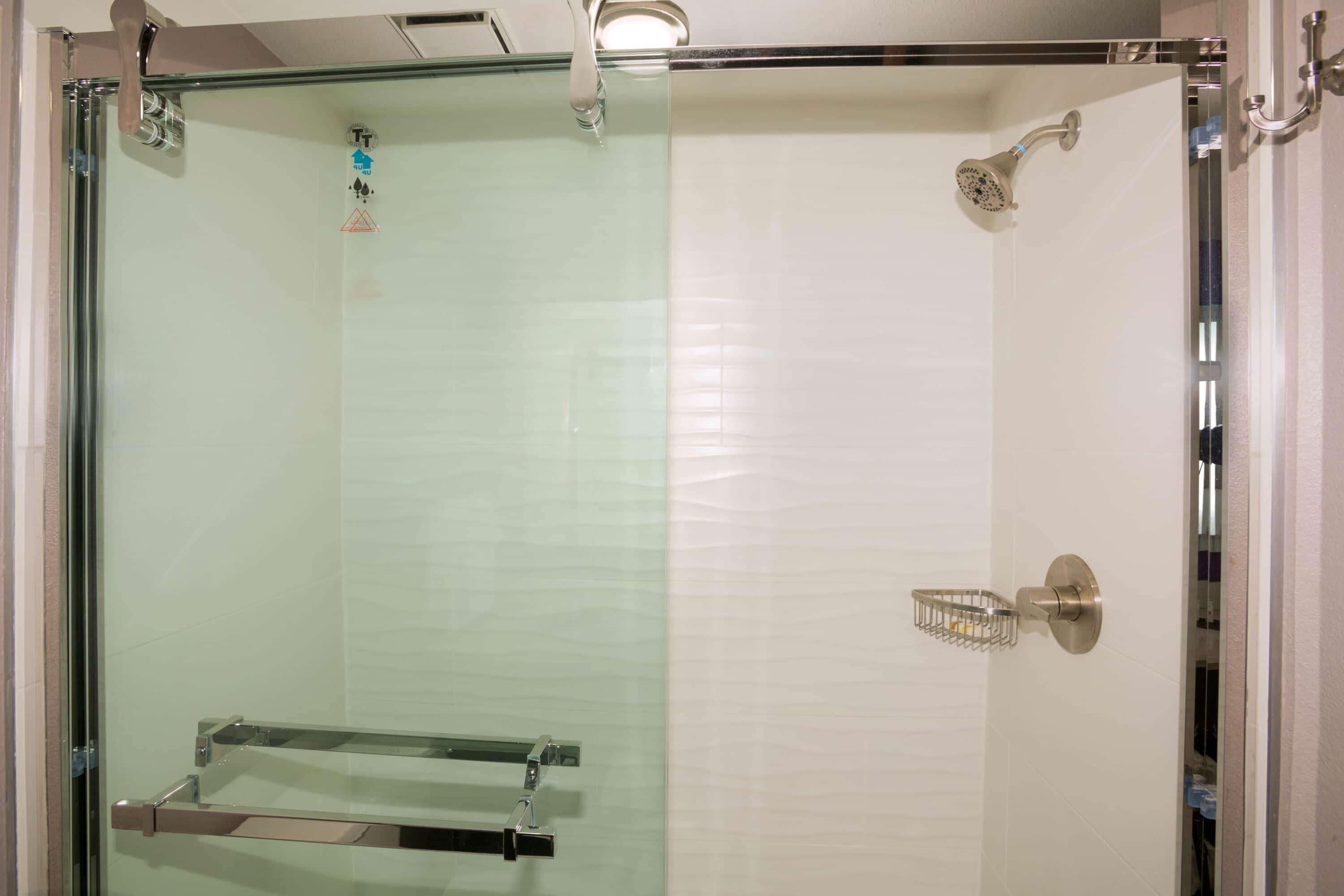 A glass-enclosed shower with a handheld showerhead and a towel rack.