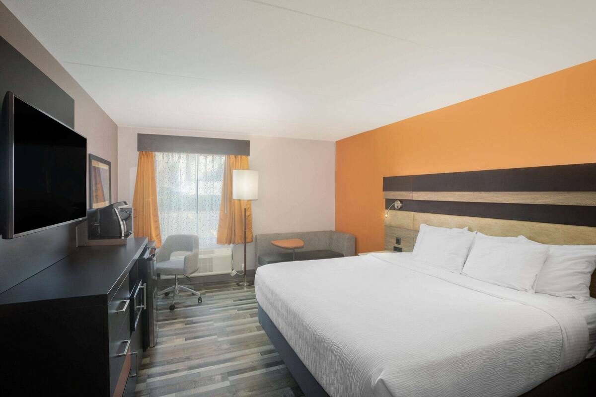 A hotel room with a bed, a desk, a chair, a TV, and a window with curtains.