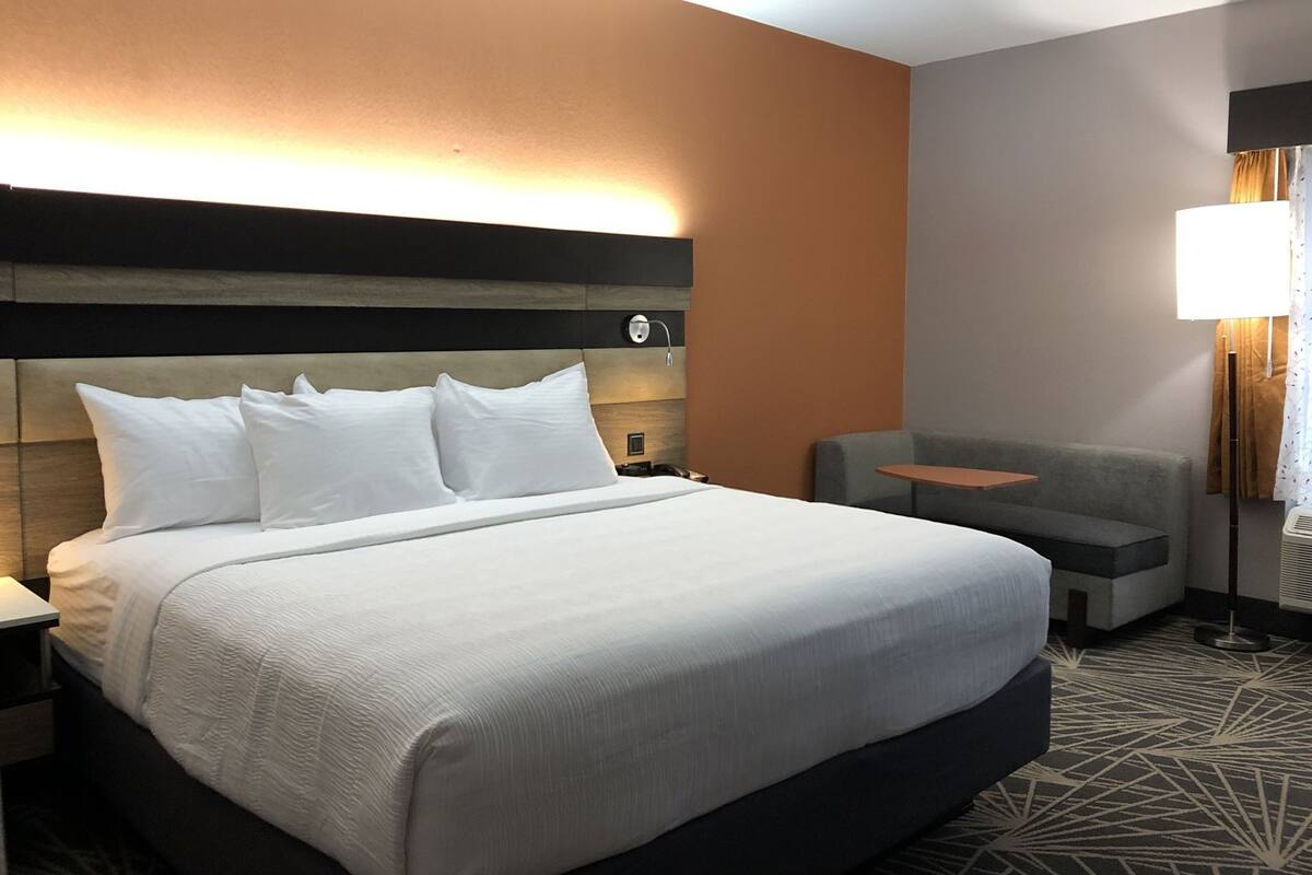 A hotel room with a large bed, a small table, a sofa, and a lamp.