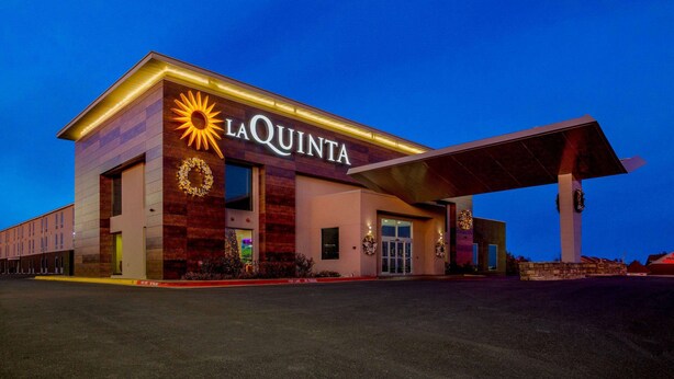 Ett La Quinta-hotell med modern design, kännetecknat av en stor solsymbol, en överbyggd entré och en parkeringsplats.