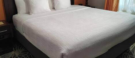 A hotel room with a large bed, a nightstand, a lamp, and a window with curtains.