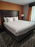 A hotel room with a large bed, a nightstand, a lamp, and a window with curtains.