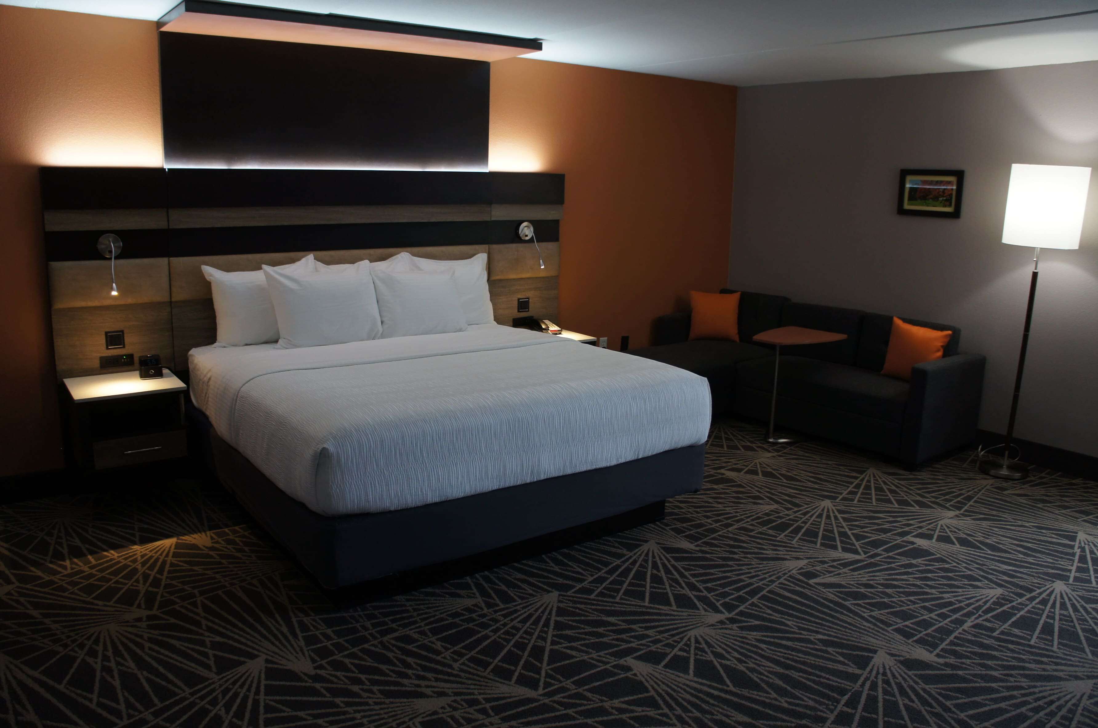 A modern hotel room with a large bed, a sofa, a desk, and a lamp.
