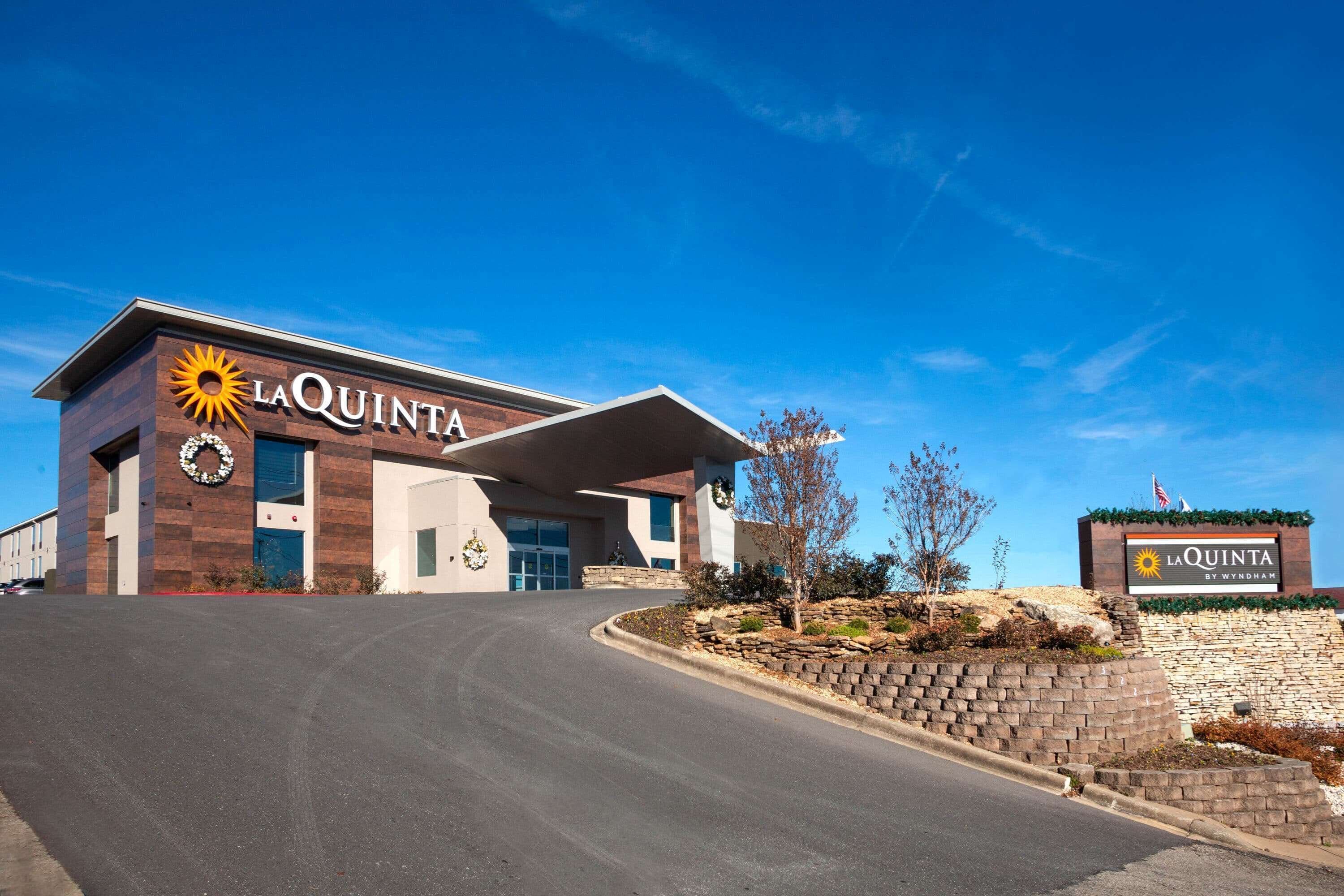 Een La Quinta hotel met een modern design, met een opvallende ingang en een aangelegde tuin met een stenen muur en planten.