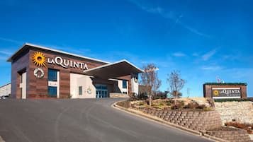 Hotel La Quinta con un diseño moderno, que presenta una entrada destacada y un área ajardinada con muro de piedra y plantas.
