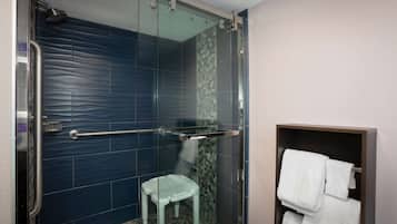 A shower with a glass door, a white step stool, and a towel rack with white towels.