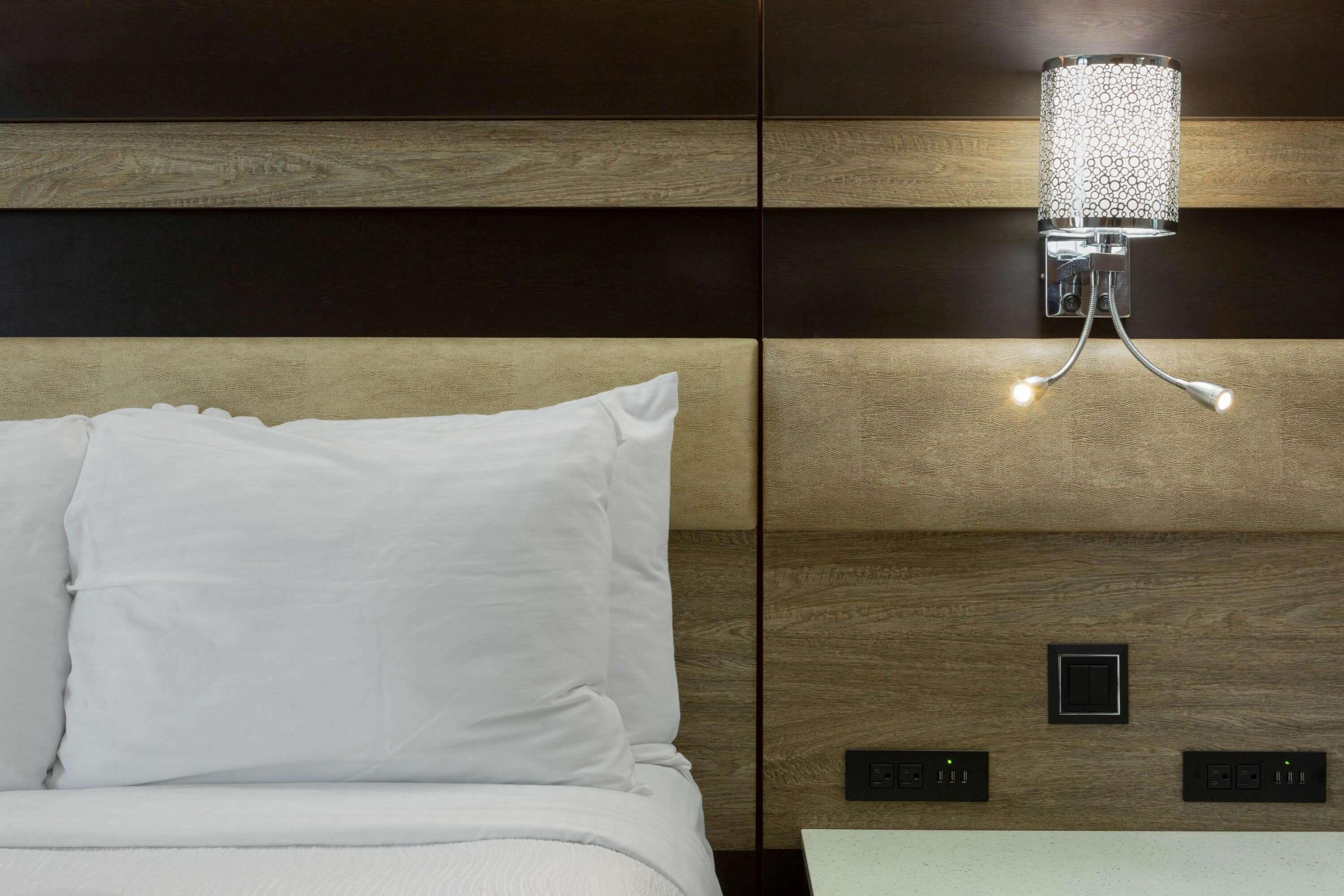 A bed with white bedding, a wall-mounted light fixture, and two control panels.