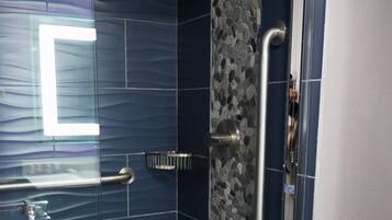 Ducha con mampara de vidrio, barandilla y suelo de azulejos.