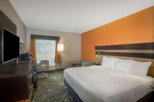 A hotel room with a large bed, a desk with a flat-screen TV, a chair, and a small table.