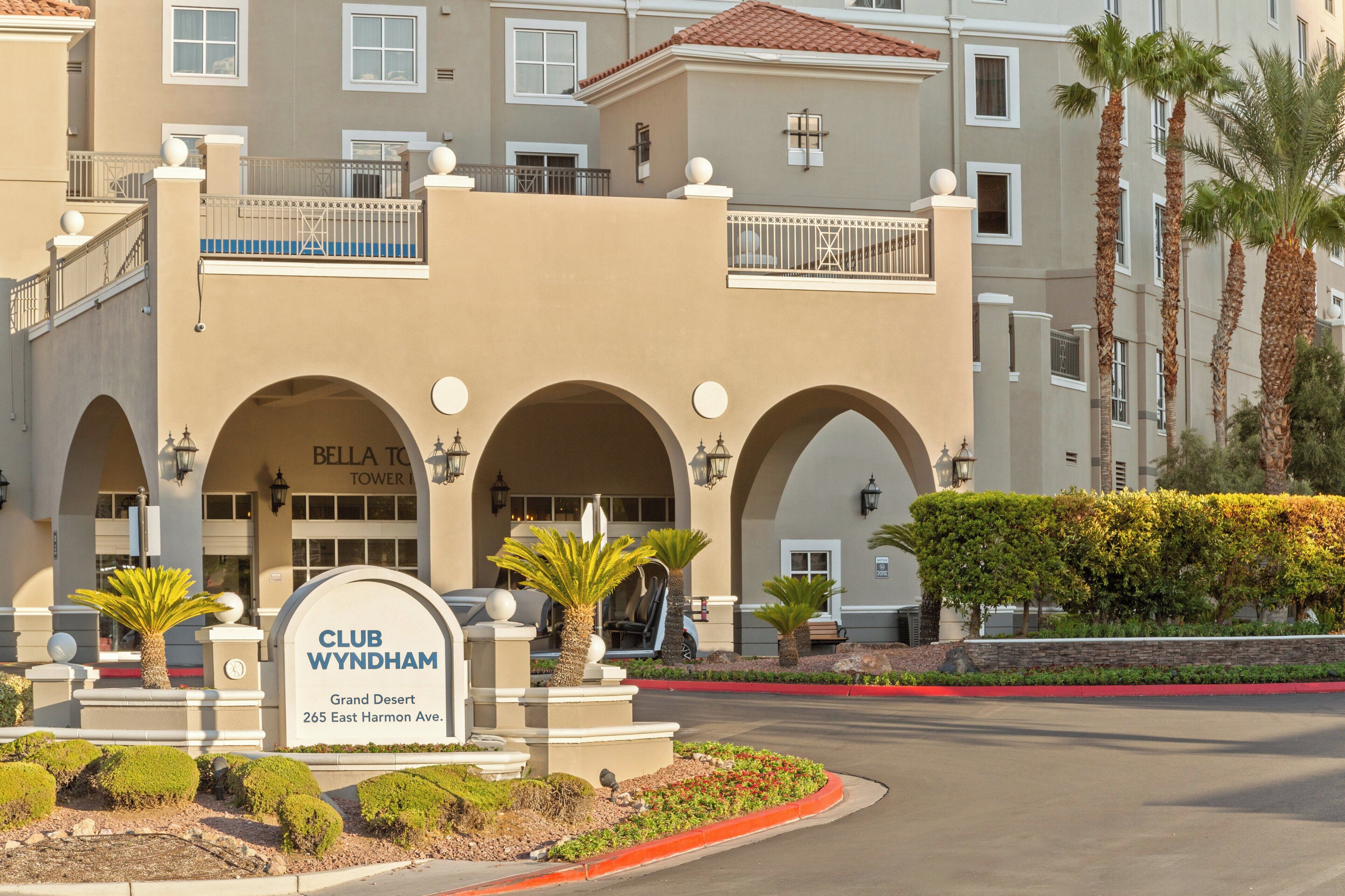 Un hotel con un cartel que dice "Club Wyndham Grand Desert 265 East Harmon Ave". Presenta un estilo arquitectónico mediterráneo con arcos y un balcón.