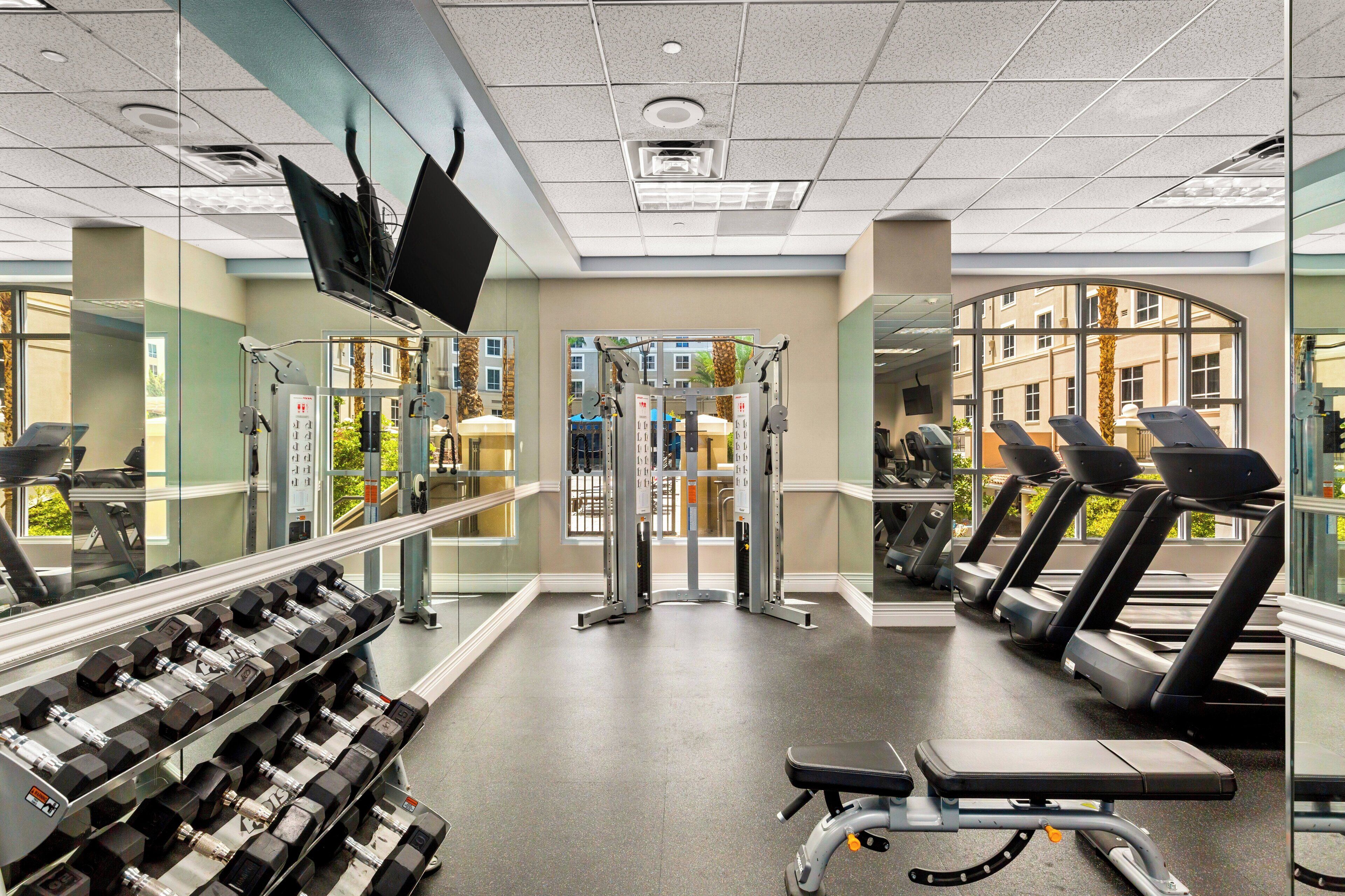 A gym with weight machines, treadmills, and a mirror wall.