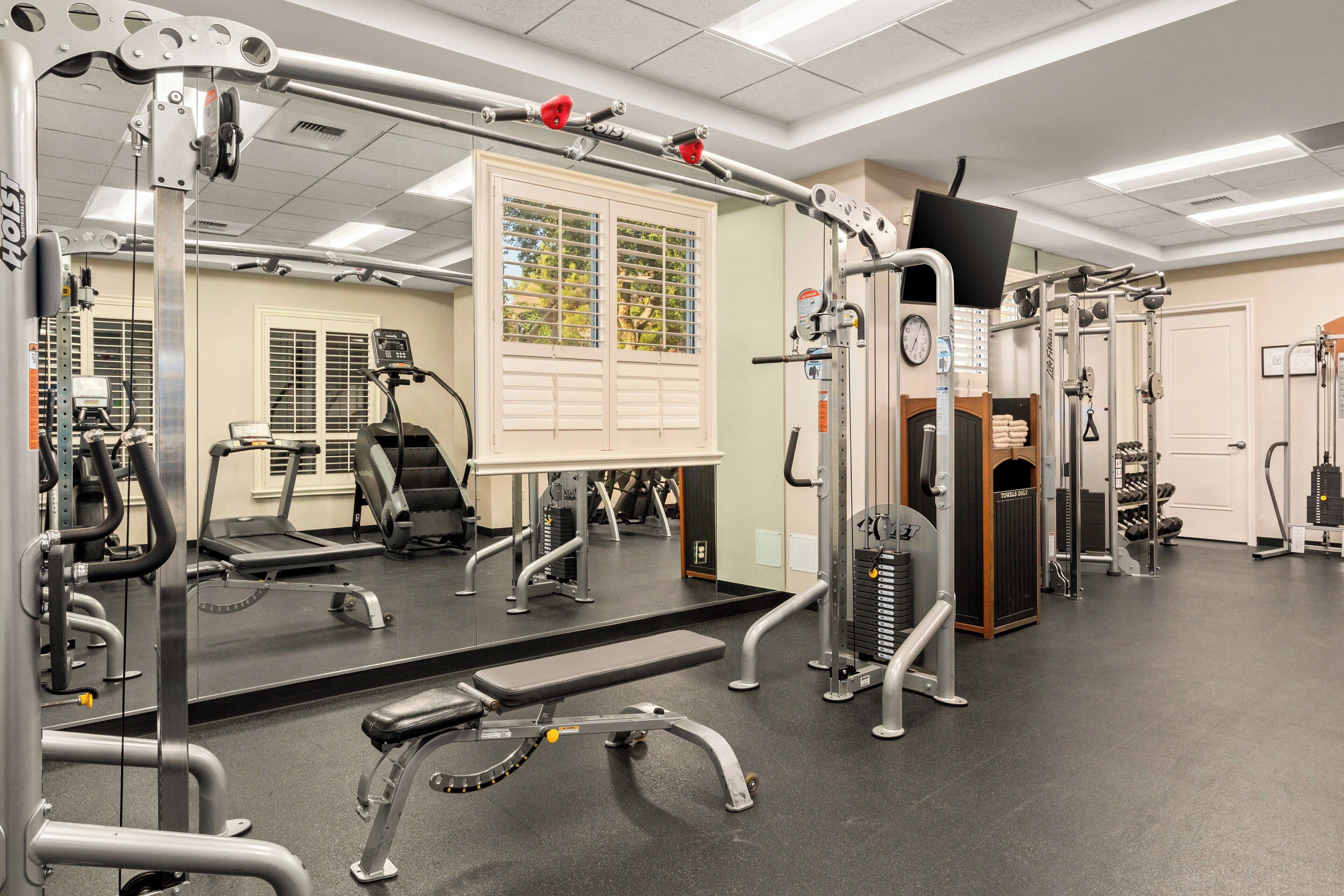 A gym with various exercise equipment, a mirrored wall, and a window with blinds.