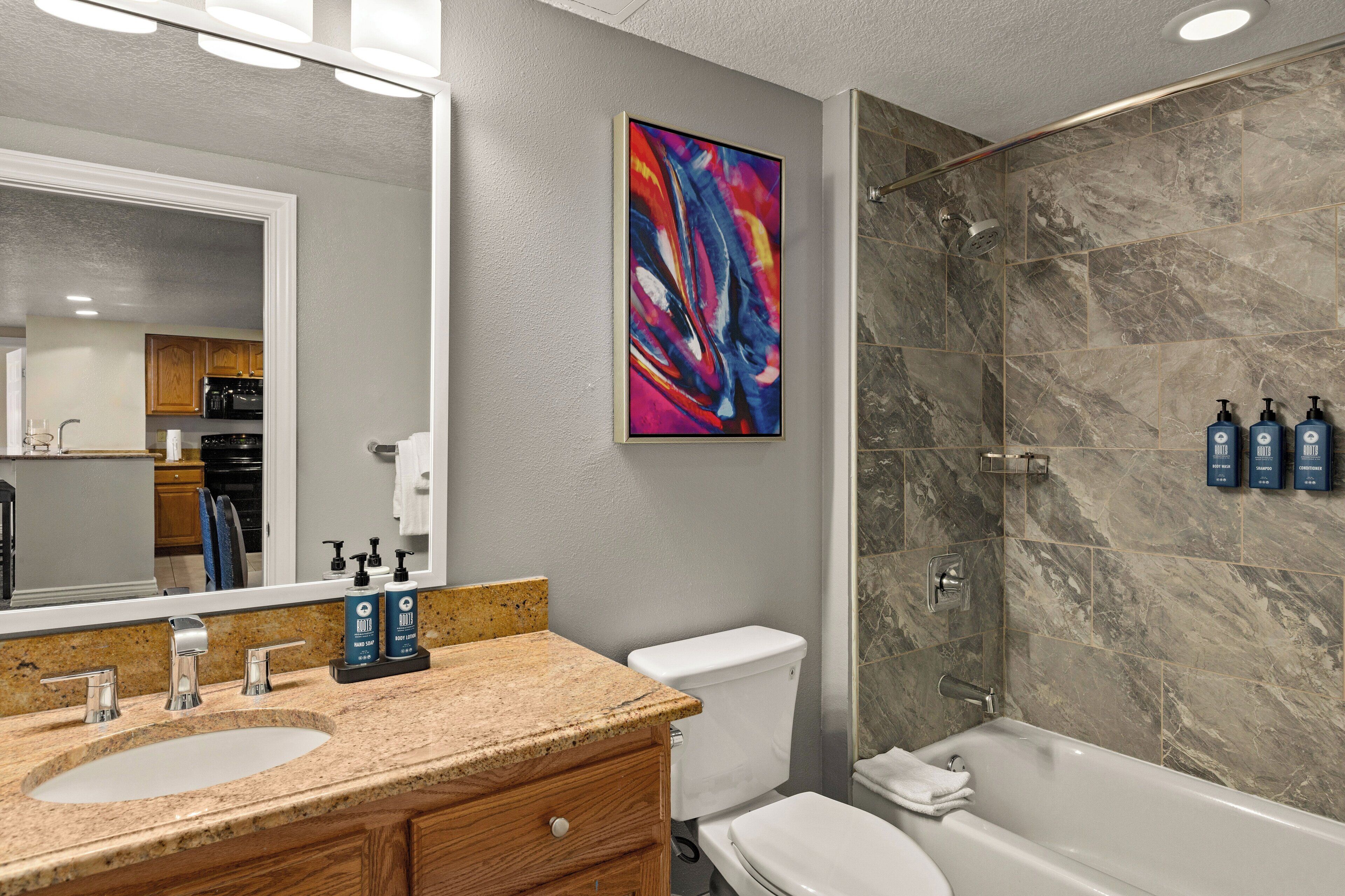 A bathroom with a granite countertop, a white toilet, a bathtub, and a shower with marble tiles.