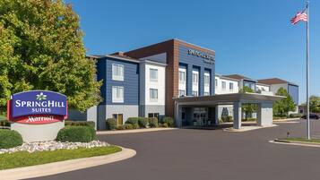 Un hotel SpringHill Suites Marriott con un diseño moderno, una entrada cubierta y un asta con la bandera estadounidense.