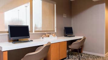 A hotel room with a long desk, two monitors, a keyboard, and two chairs.