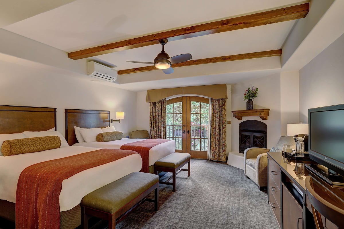 A hotel room with two beds, a television, a fireplace, and a large window with curtains.