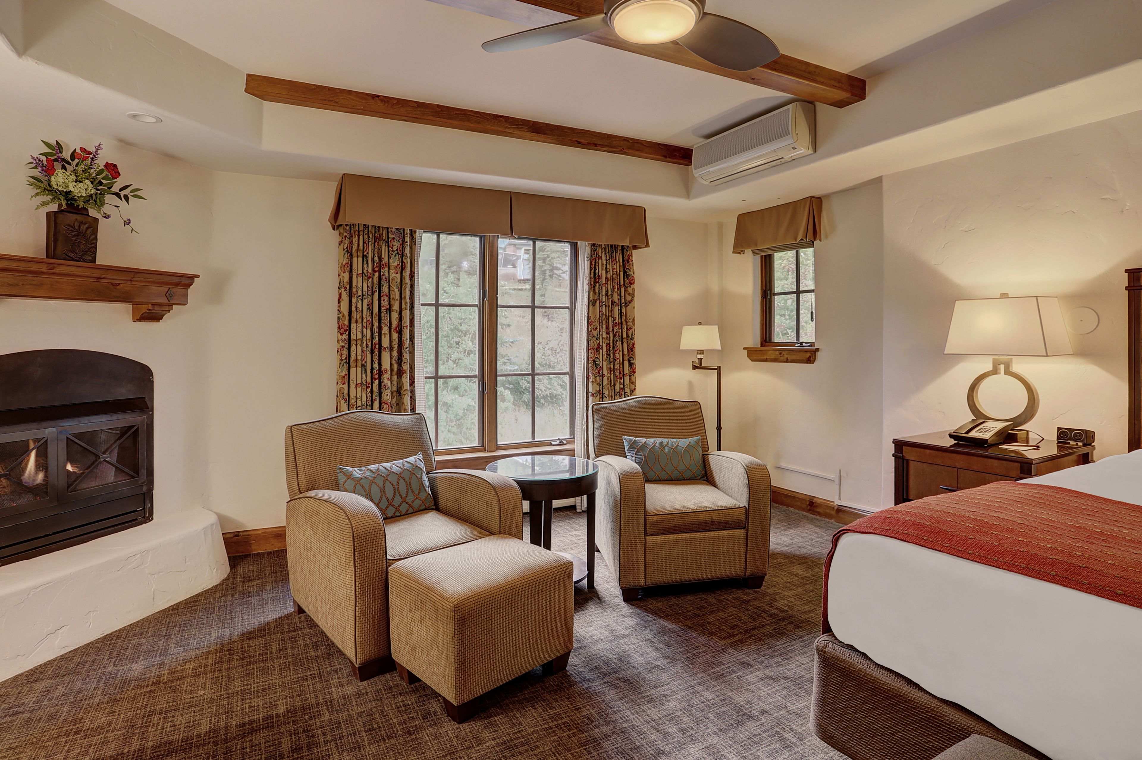 A hotel room with a fireplace, two armchairs, a bed, and a small table.