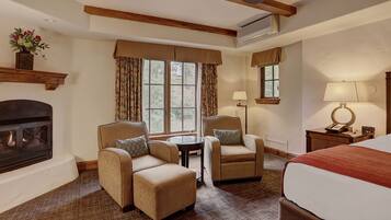 A hotel room with a fireplace, two armchairs, a bed, and a small table.