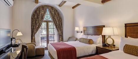 Une chambre d’hôtel avec deux lits, un bureau avec une chaise, une télévision et une fenêtre avec des rideaux.
