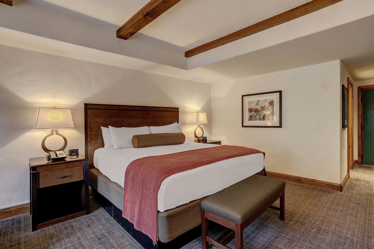 A hotel room with a large bed, two bedside tables with lamps, a bench, and a framed picture on the wall.