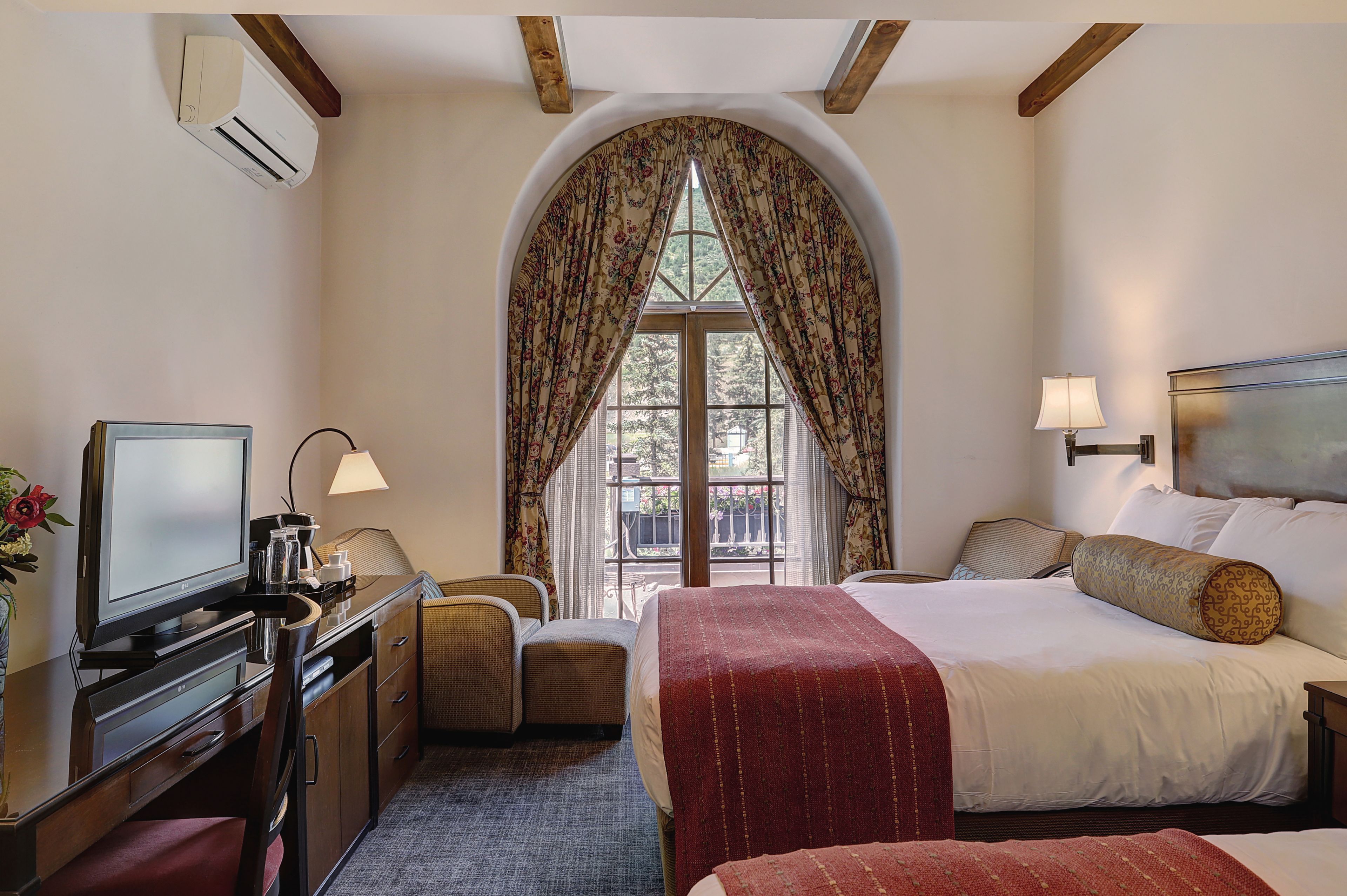 A hotel room with a bed, a desk with a television, a chair, and a window with curtains.
