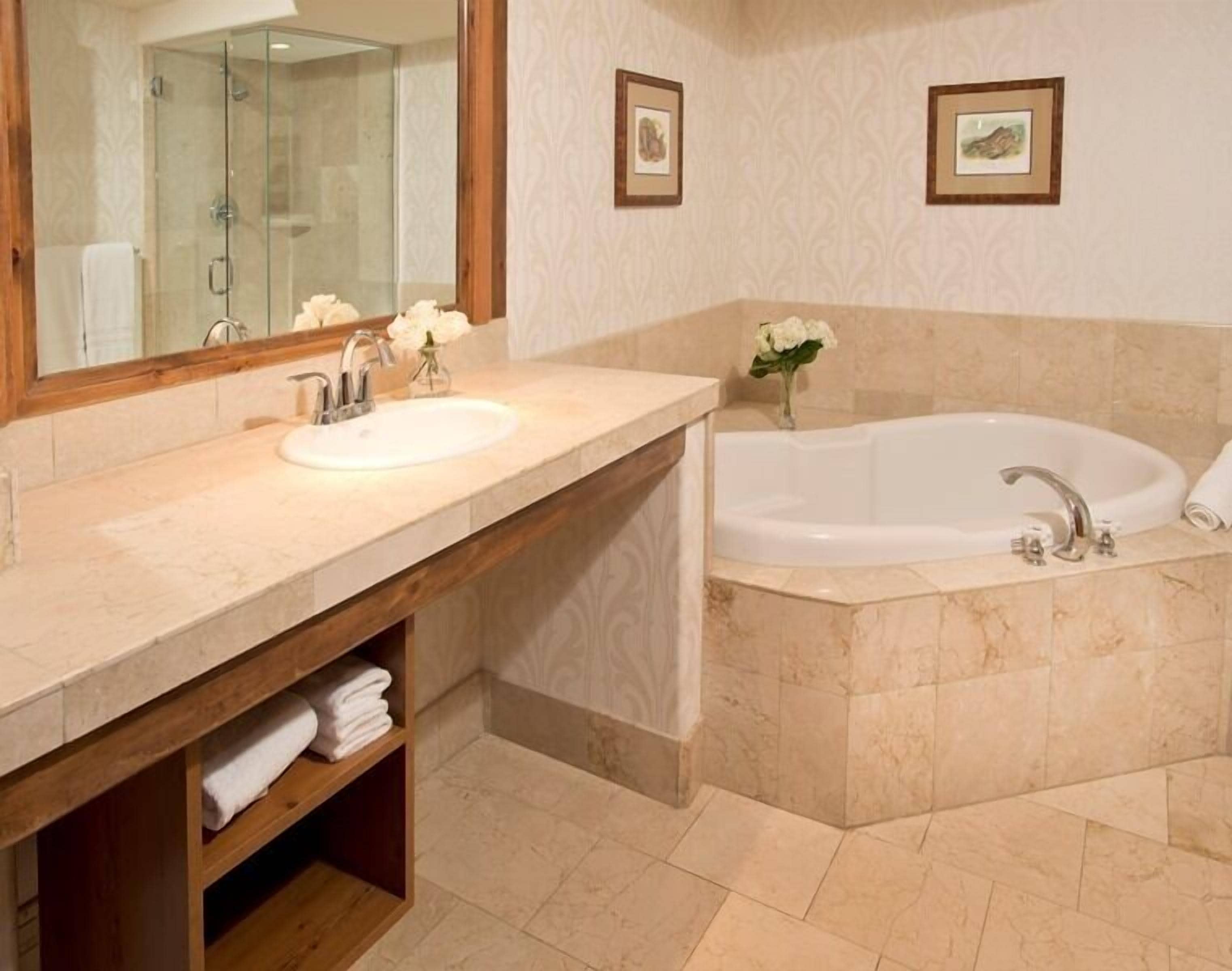 A bathroom with a glass shower enclosure, a sink with a mirror, a bathtub, and two framed pictures on the wall.