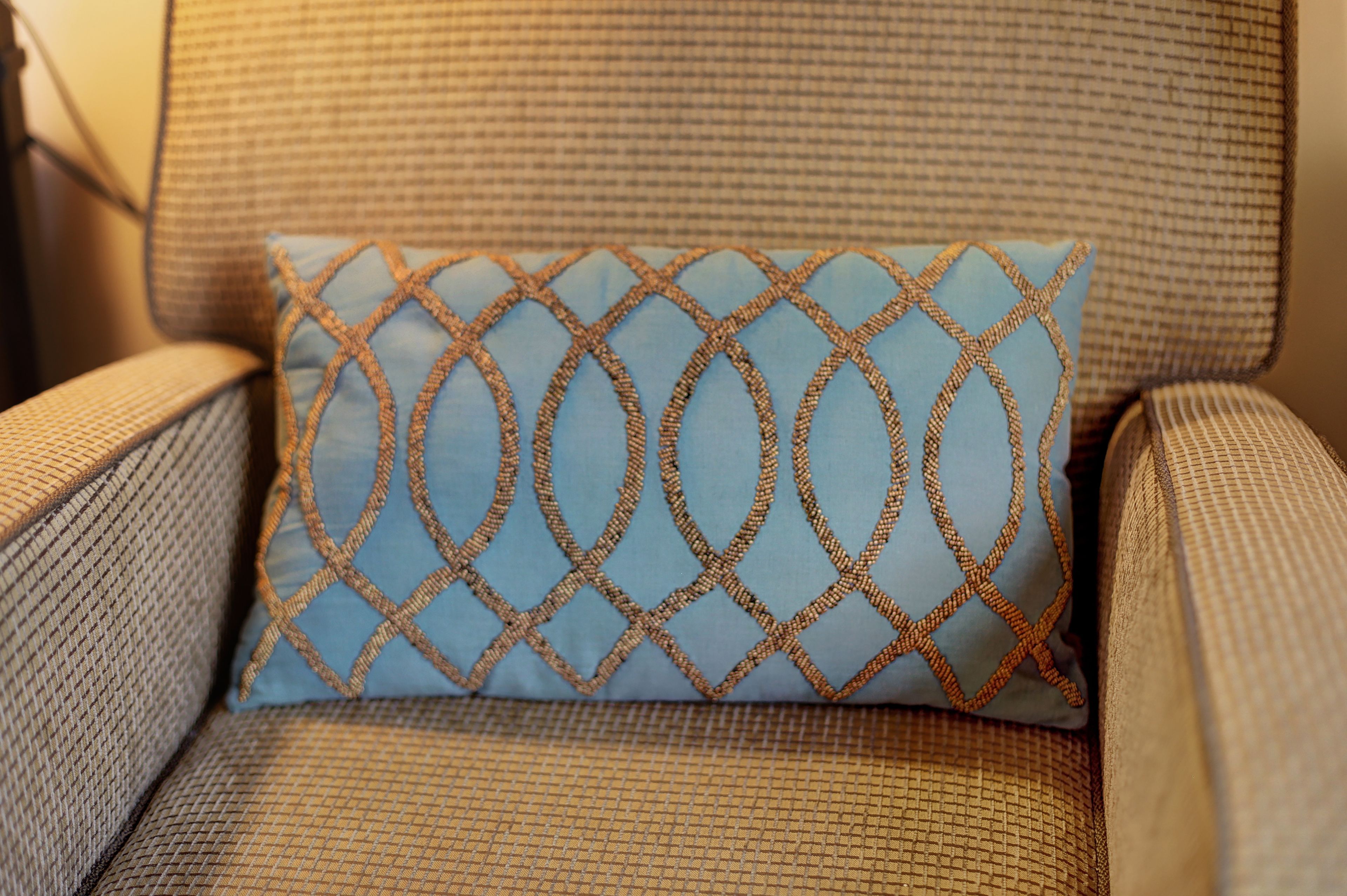 A close-up of a chair with a textured fabric and a decorative pillow with a geometric pattern.