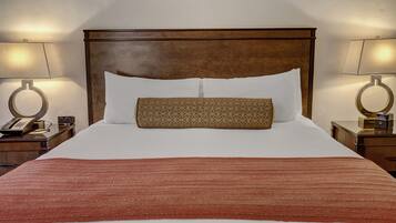 A neatly made bed with a patterned pillow and a red blanket, flanked by two bedside tables with lamps and a telephone.