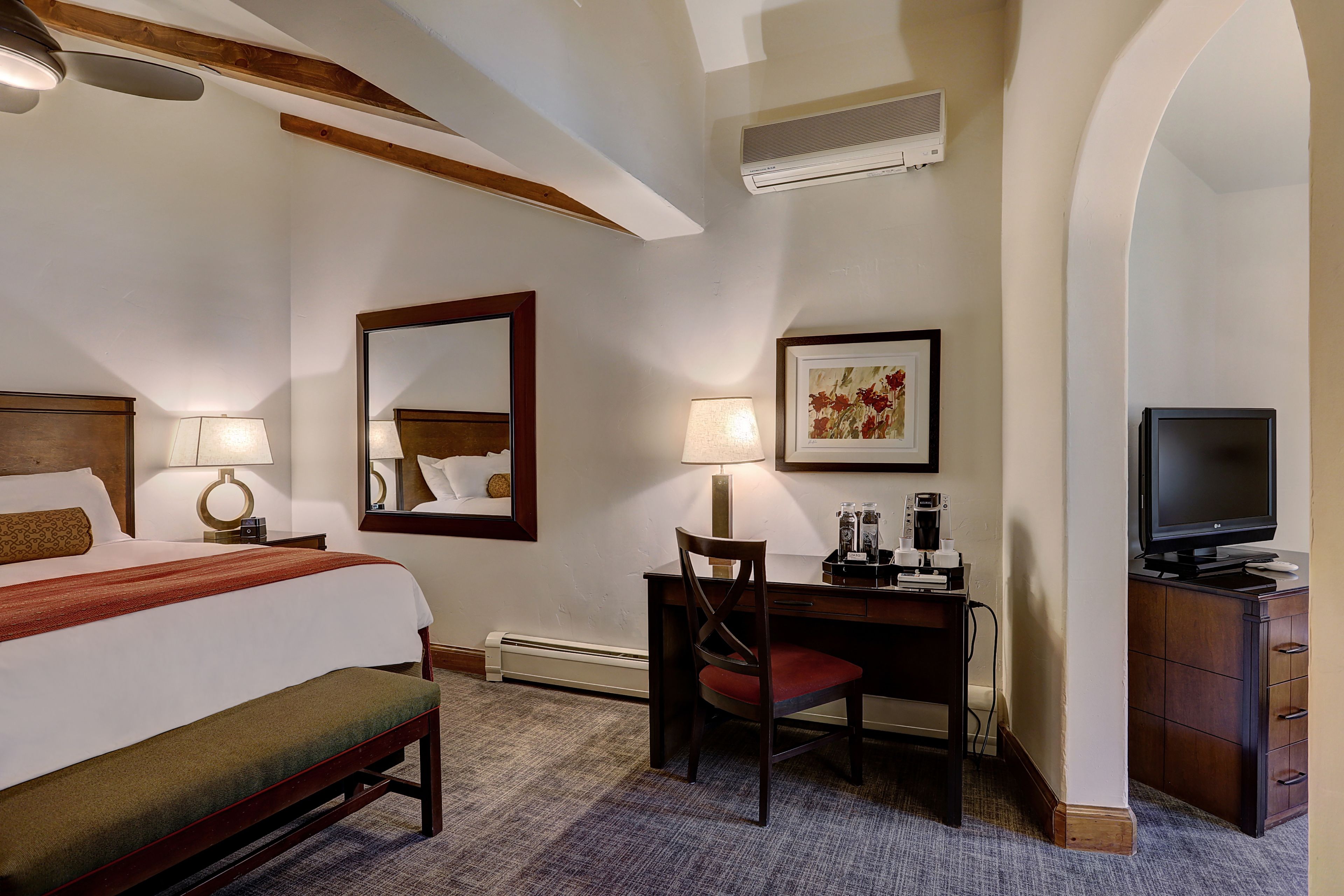A hotel room with a bed, desk, chair, television, and a mirror.