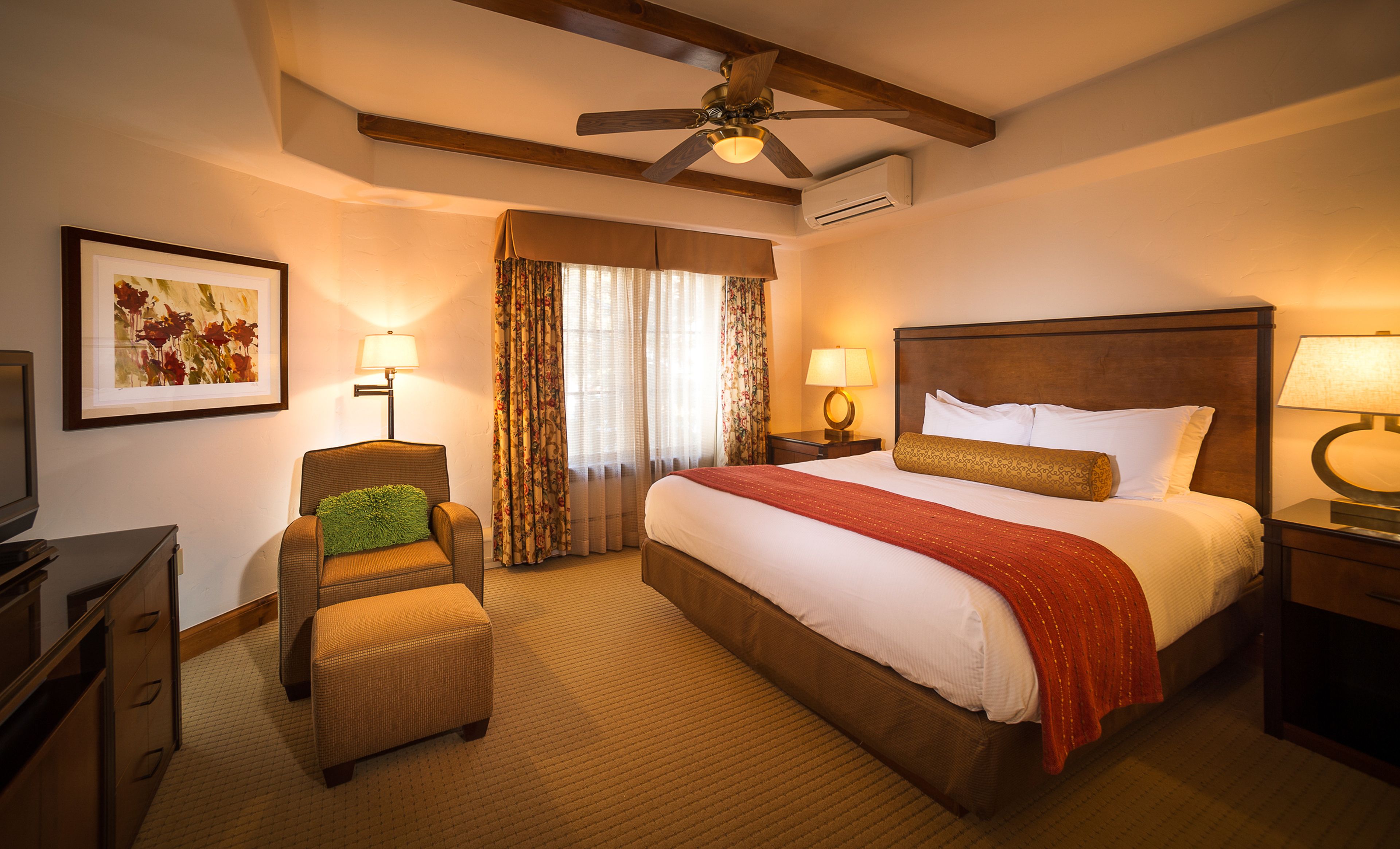 A hotel room with a large bed, a chair, a desk, a ceiling fan, and a window with curtains.