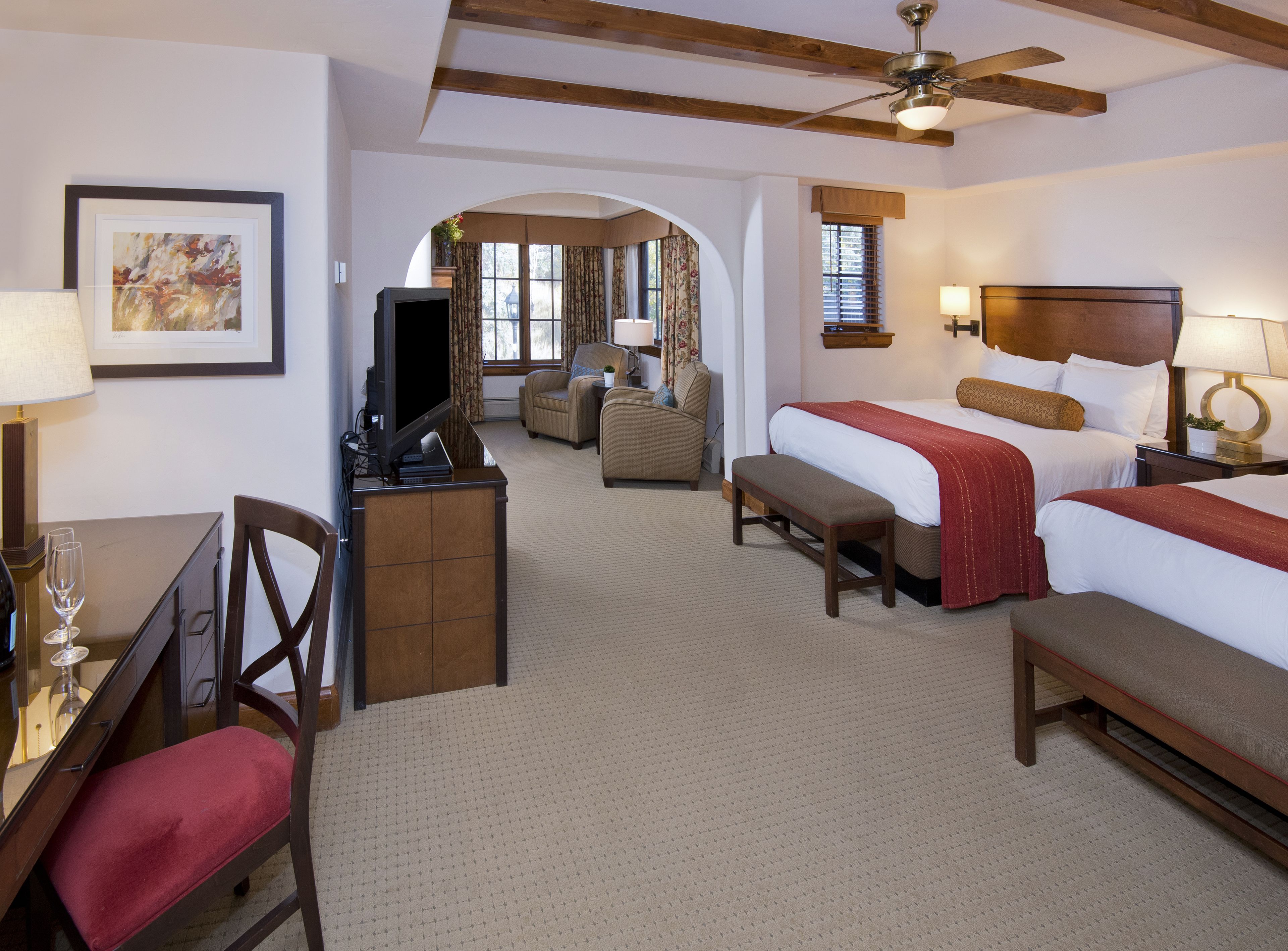 A hotel room with two beds, a desk with a television, a chair, and a sofa.