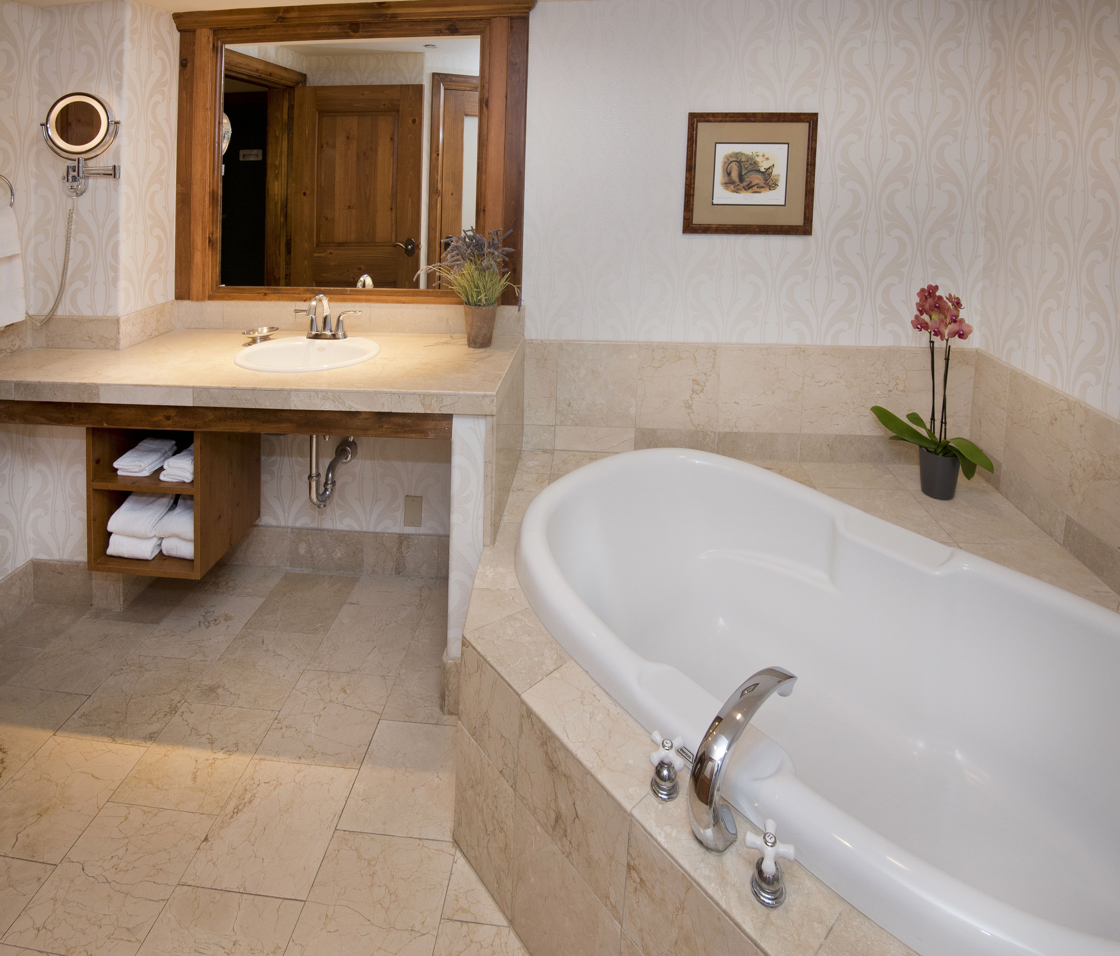 A bathroom with a large bathtub, a sink with a mirror, and a wooden shelf with towels.