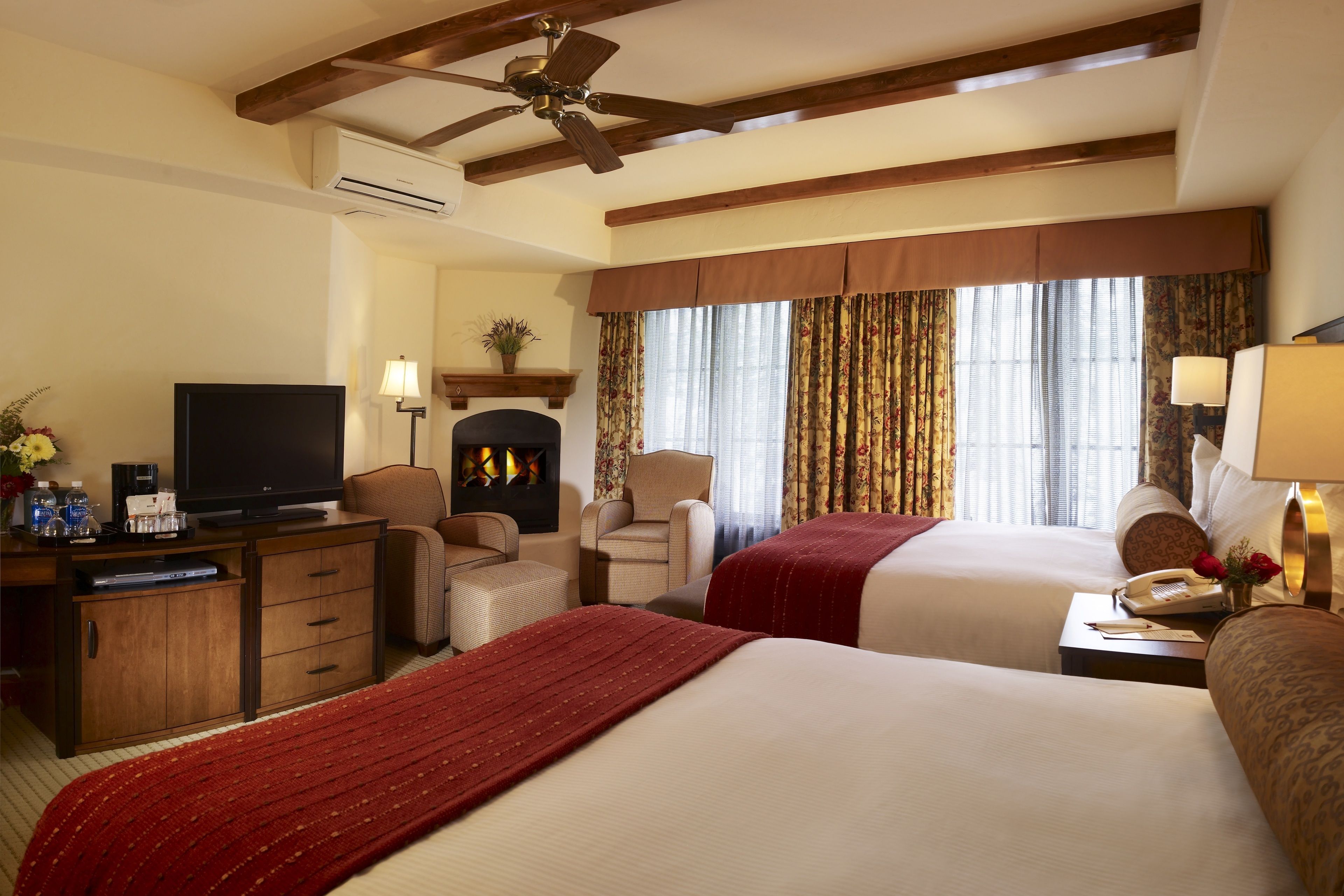 Une chambre d’hôtel avec deux lits, une télévision, une cheminée, un bureau avec un téléphone et un ventilateur de plafond.