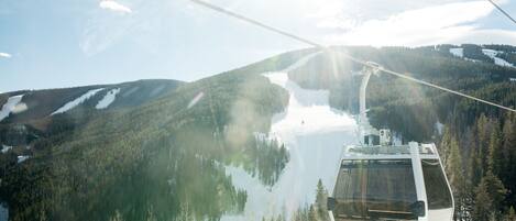 A cable car moving over a forested mountain with a clear sky.