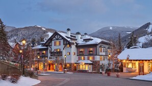 Un hotel grande de varios pisos con un estilo arquitectónico europeo tradicional, que destaca por su entrada imponente, múltiples balcones y un paisaje nevado al fondo.