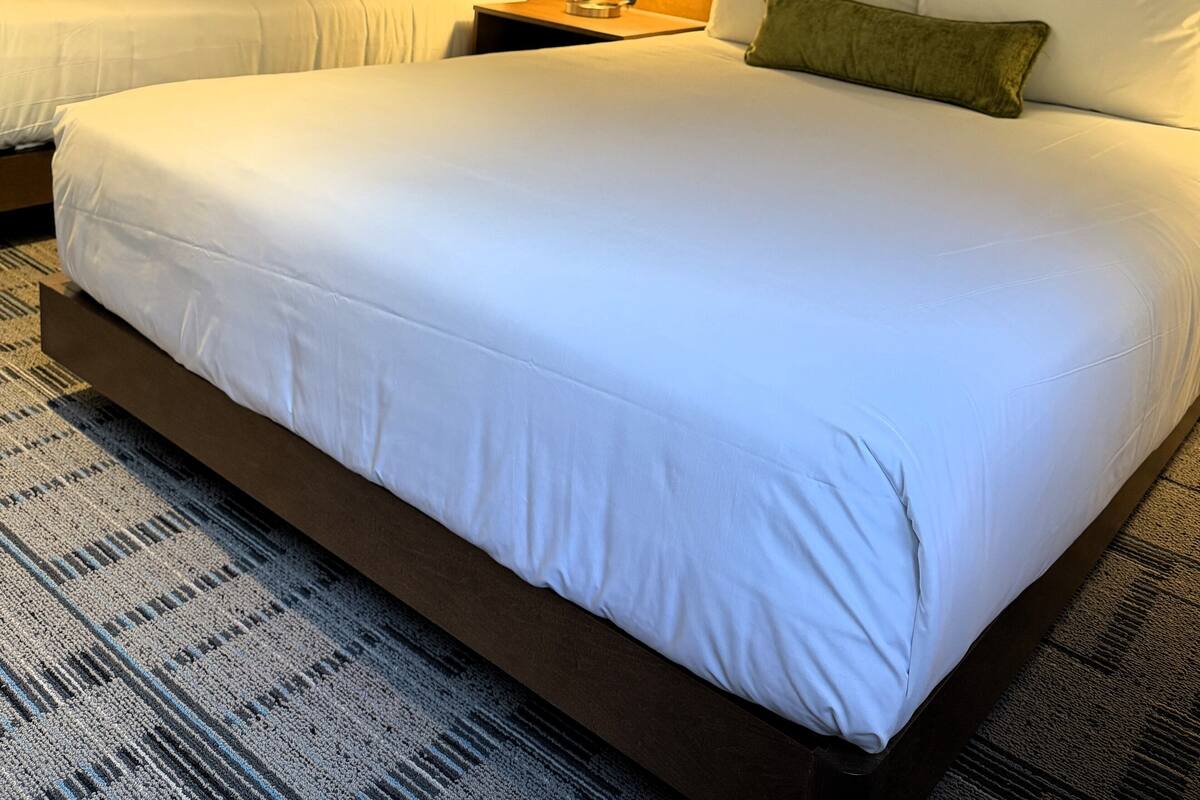 A hotel room with two beds, a nightstand with a lamp, and a patterned carpet.