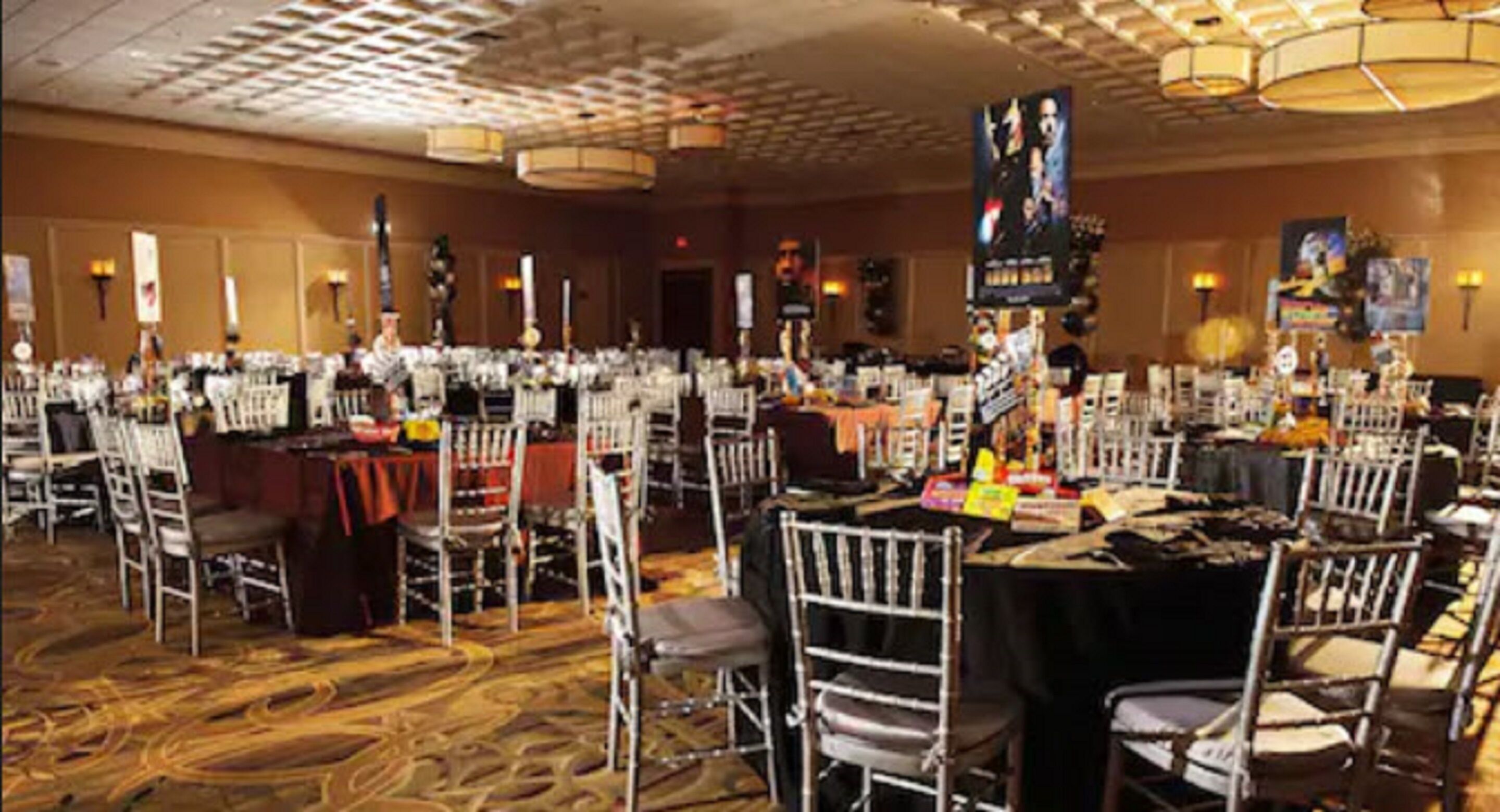 Un salón de banquetes con mesas redondas, sillas blancas y piso alfombrado.