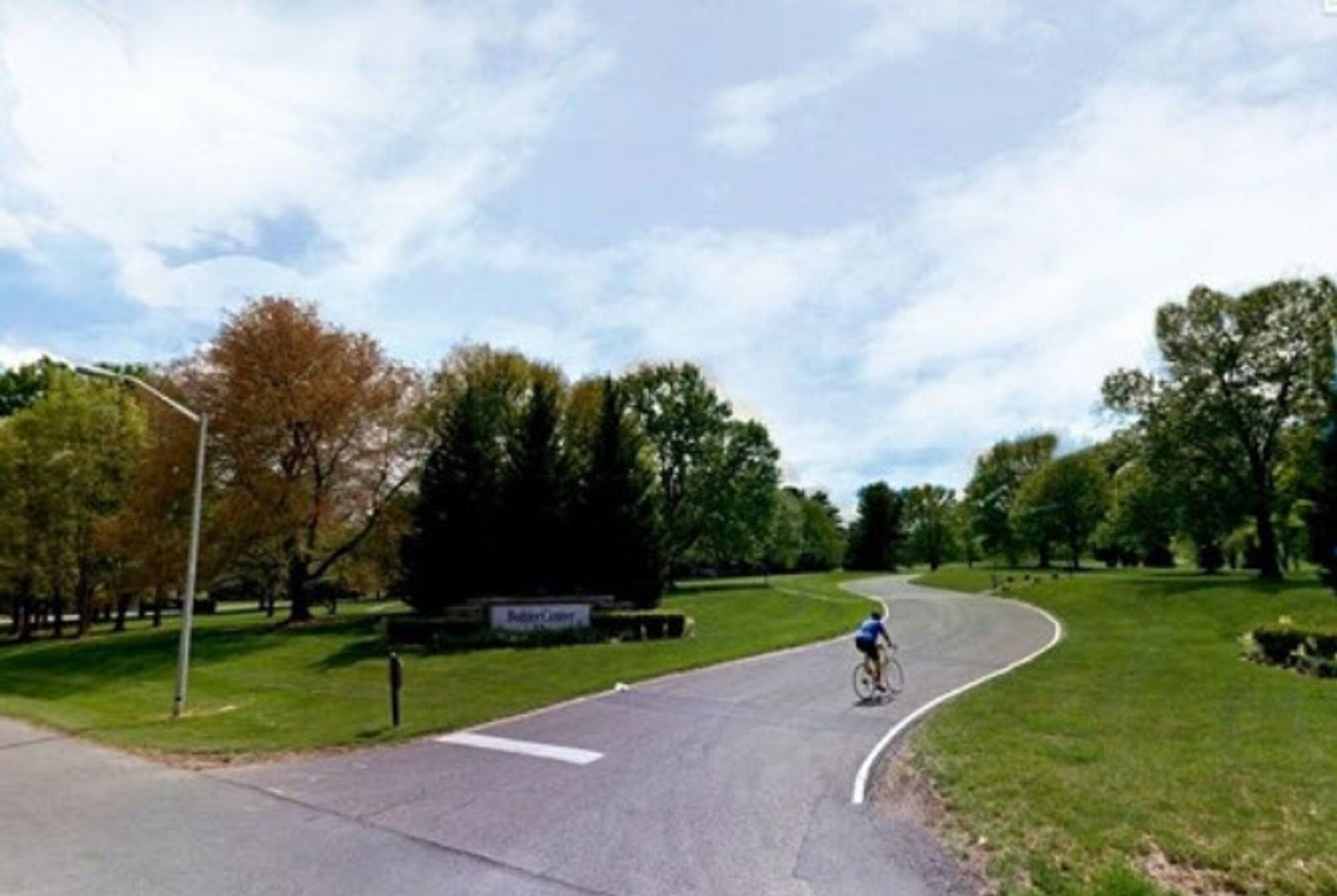 Una carretera sinuosa con un ciclista, rodeada de árboles y zonas verdes.