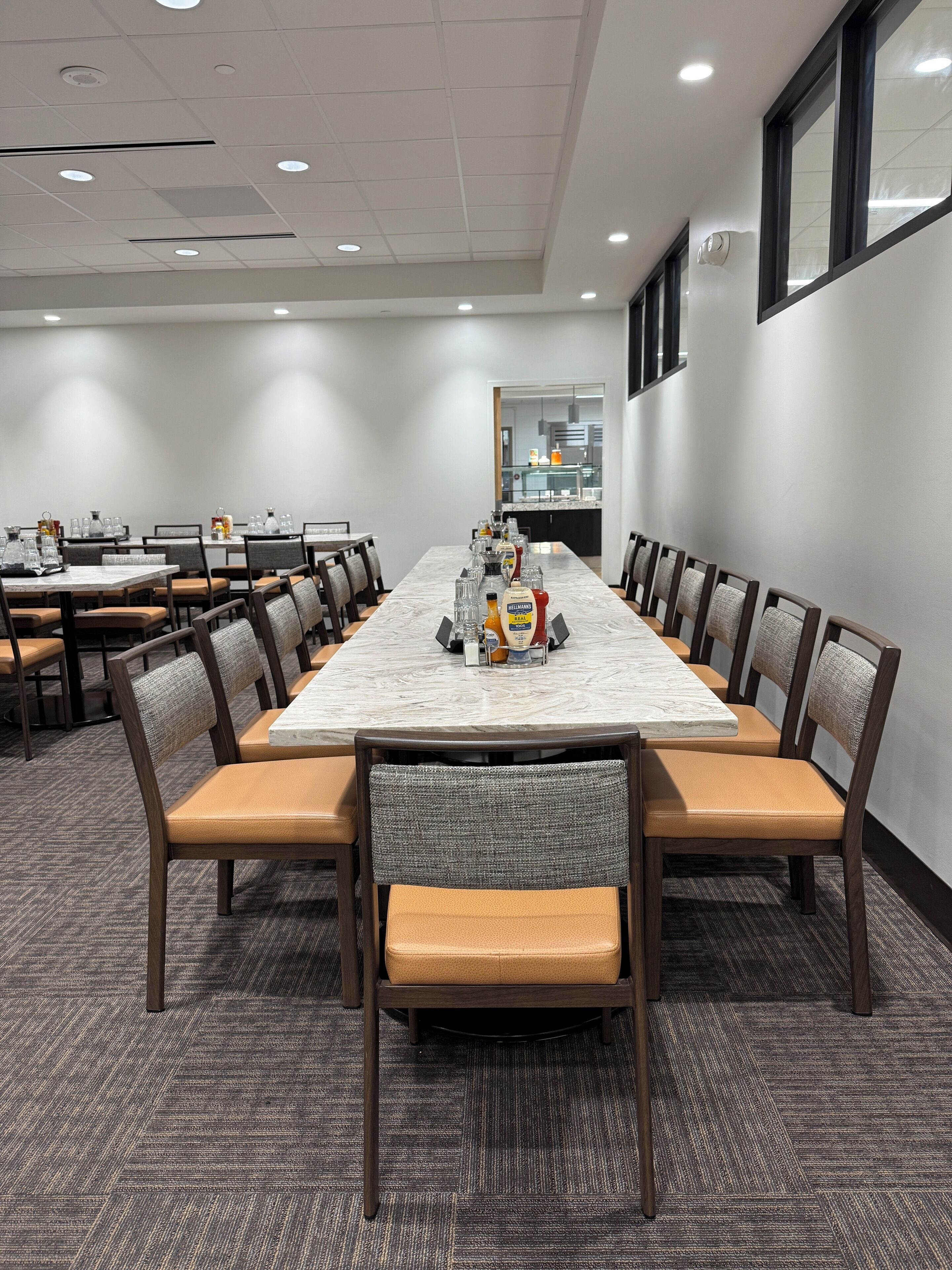 A conference room with a long table, chairs, and a kitchen area visible through a doorway.