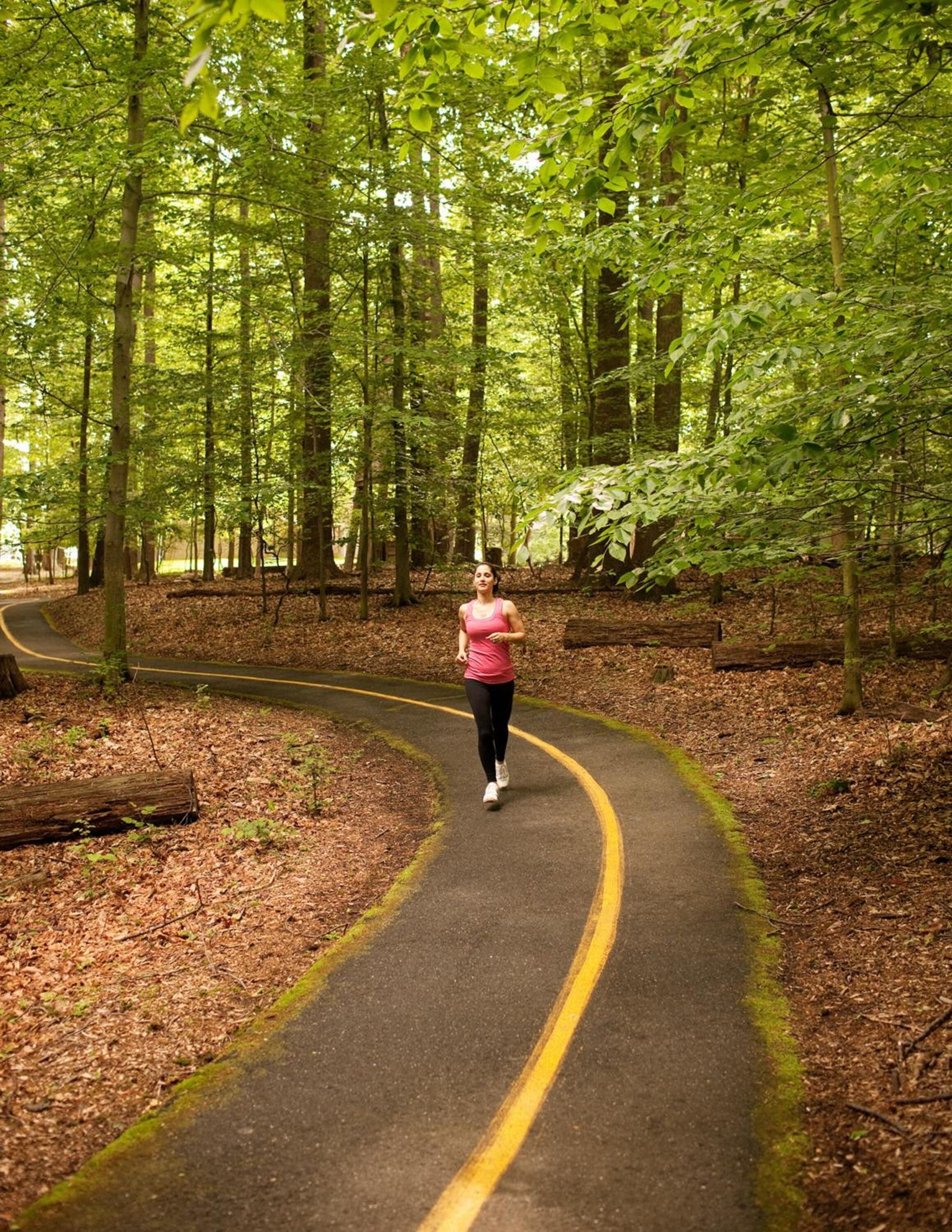 Una mujer trotando por un sendero pavimentado rodeado de árboles en un bosque.