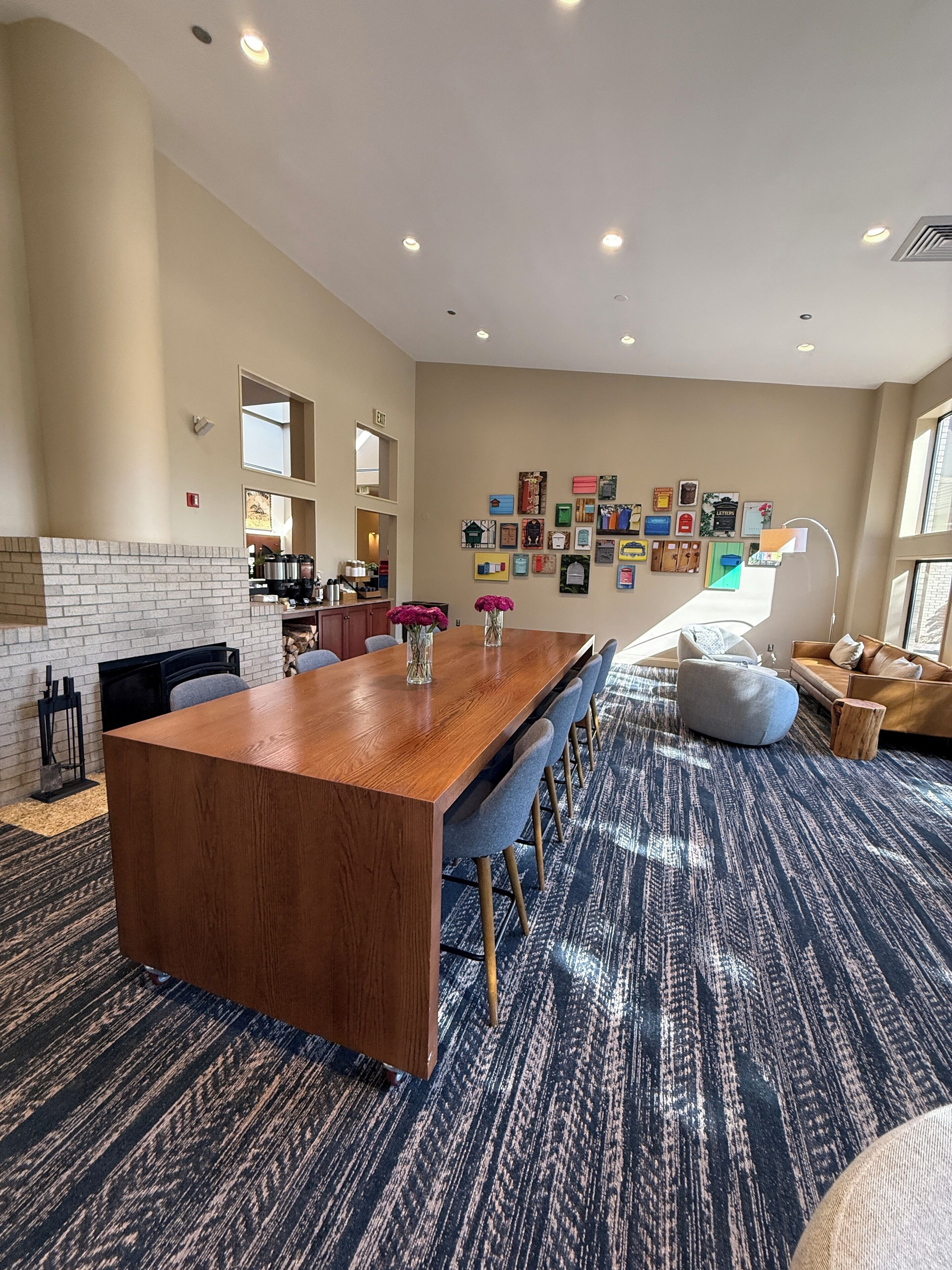 Quarto de hotel moderno com mesa de jantar de madeira, carpete estampado em azul e área de estar aconchegante com um bean bag e um sofá.