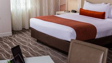 Une chambre d’hôtel avec un lit, un bureau doté d’une lampe, une chaise et une petite plante.