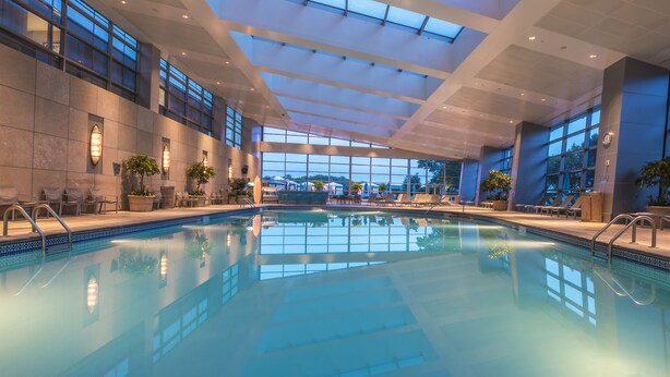 A large indoor swimming pool with clear blue water, surrounded by lounge chairs and potted plants, with a high ceiling and large windows. - Mohegan Sun (Montville)