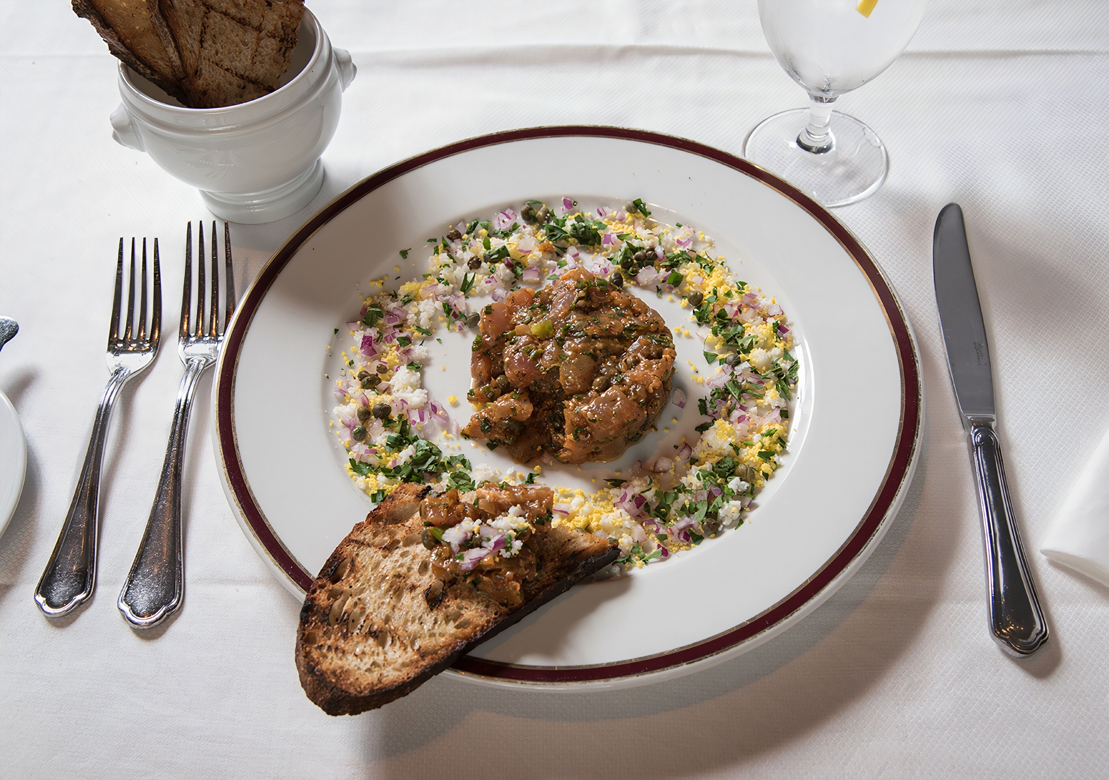 A plate with a meat dish, a slice of bread, and a glass of water on a table.