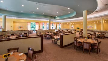 A spacious hotel lobby with multiple dining areas, partitioned seating, and a central open space.