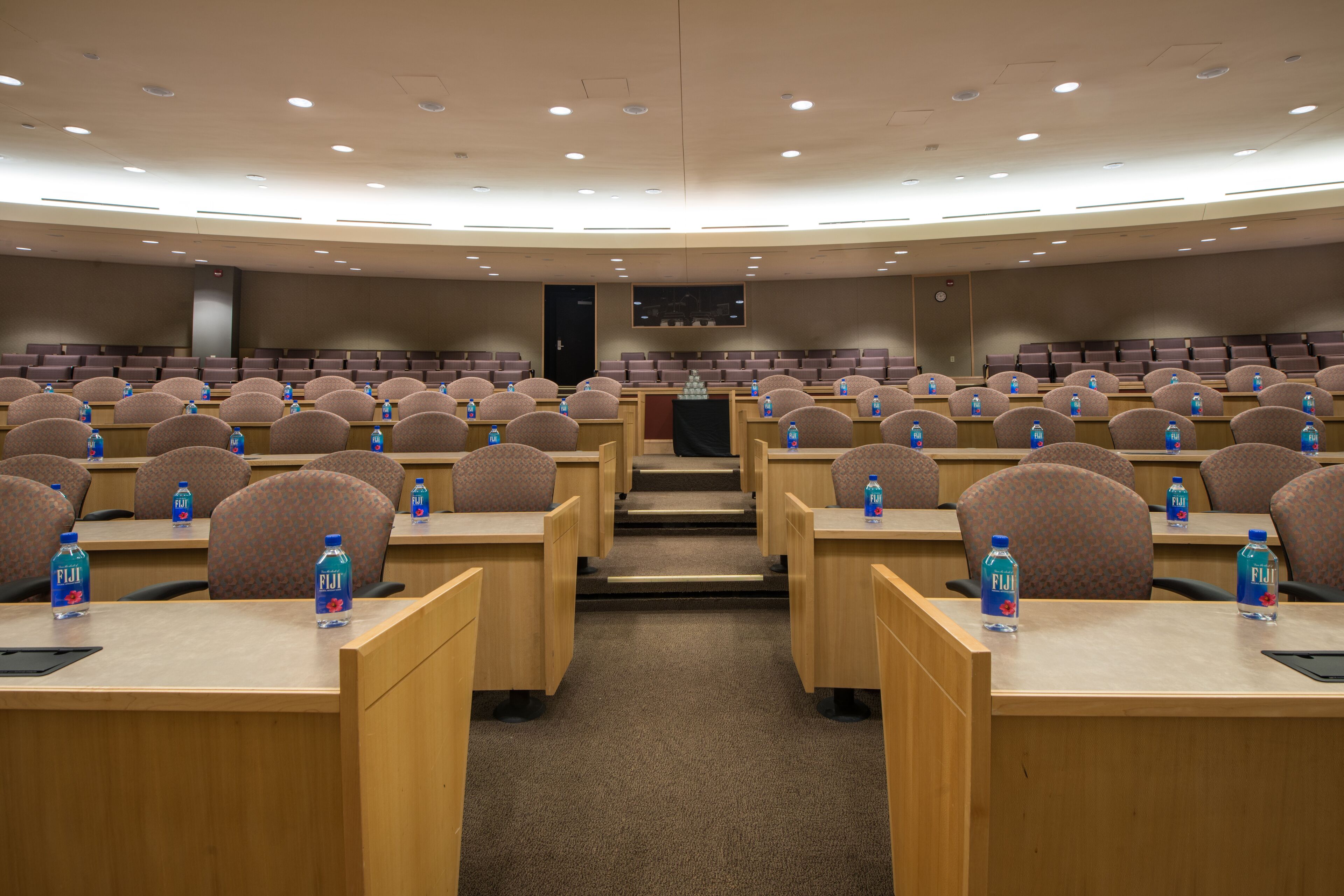 A conference room with rows of chairs and tables, each with a water bottle.