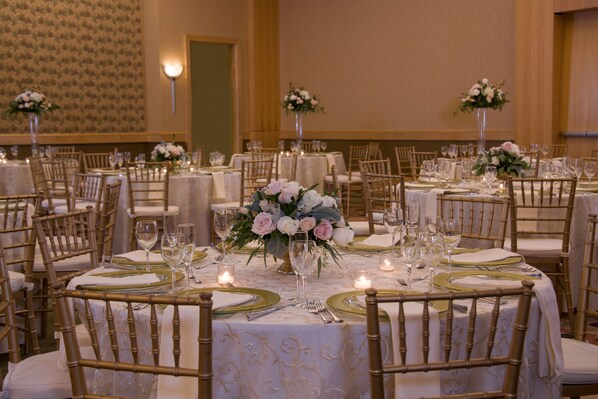 Un salón de banquetes con mesas redondas dispuestas para comer, cada una con un centro de mesa floral y velas.