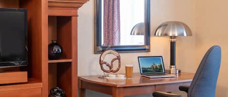 Habitación de hotel con un escritorio de madera, una laptop, un televisor, una lámpara y una silla.