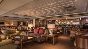 A spacious hotel lobby with a bar area, multiple seating arrangements, and a television screen.