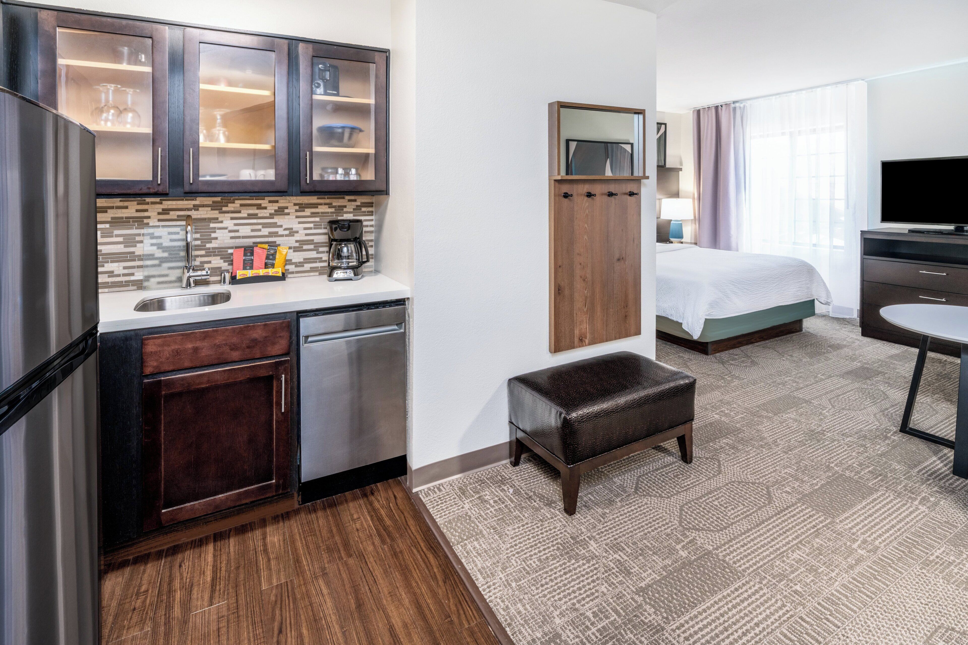 A compact hotel room with a kitchenette, a bed, a TV, and a small seating area.